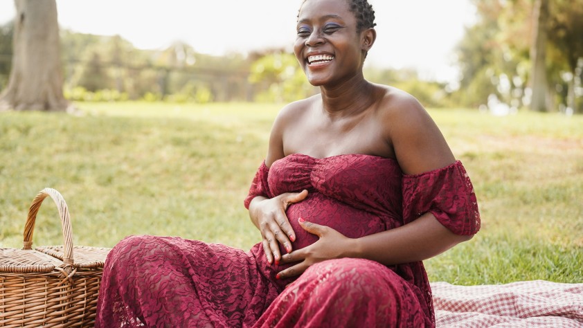 Young african pregnant woman touching her belly outdoor at city park - Focus on face